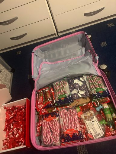 A suitcase half filled with items like sweets, candy canes, candles and cellophane bags