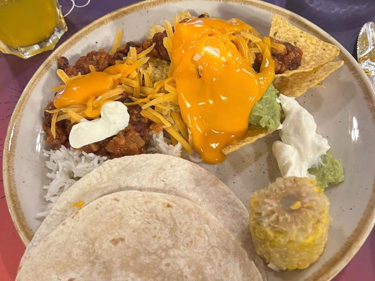 Image shows a plate of food including rice, a wrap, nachos, vegan chilli, cheese, guacamole and sweetcorn