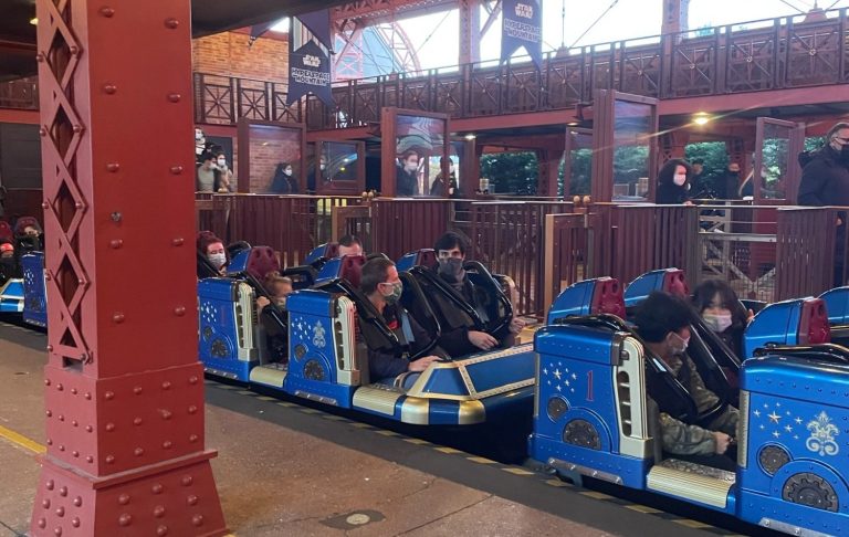 Image shows the ride vehicle in the station ready to depart, the vehicle is blue and passangers are seated with over shoulder restraints in place