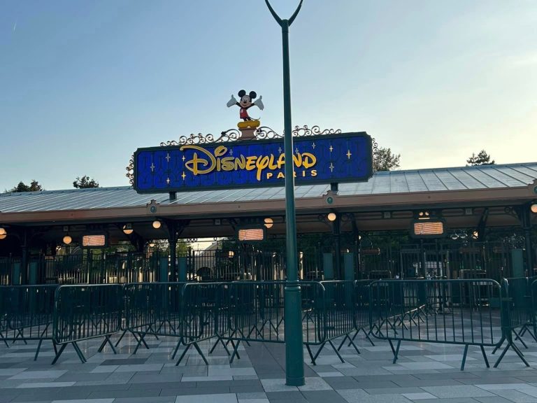 Image shows the security entrance to disney park with queue barriers and the disneyland paris sign 