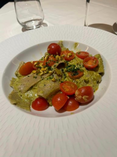 A white shallow bowl fileld with pasta covered in a green pesto sauce and with cherry tomatoes