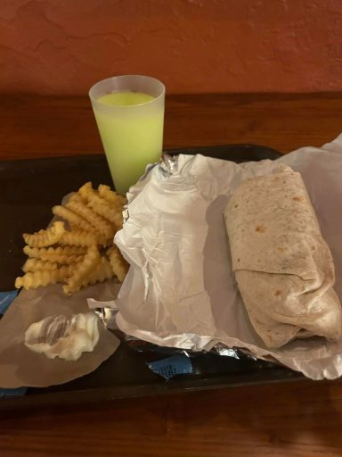 A burrito, some crinkle fries and a plastic cup filled with frozen margharita