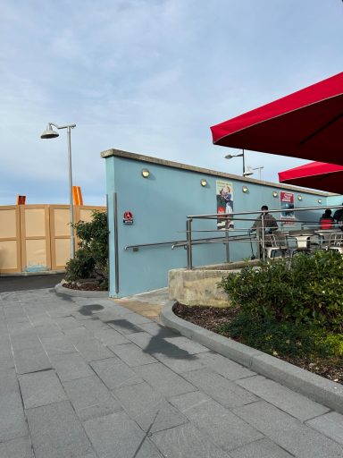 there is a pale blue wall with silver metal handrails and a ramp up to an area with red parasols