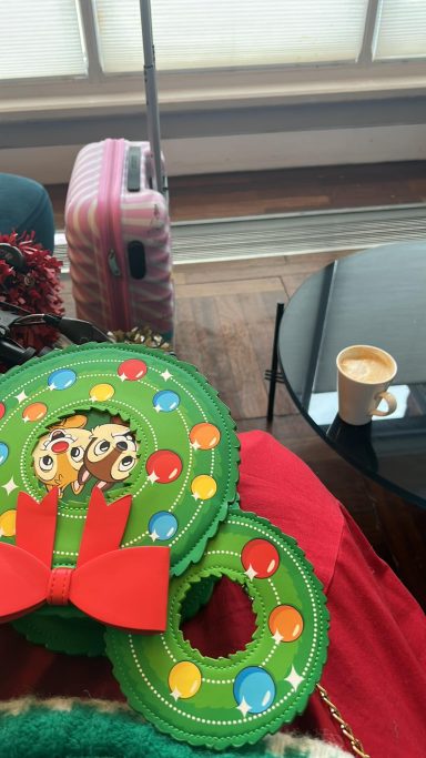 Image showing a green wreath themed bag on my lap with a coffee on a nearby table and my cabin case in front of me