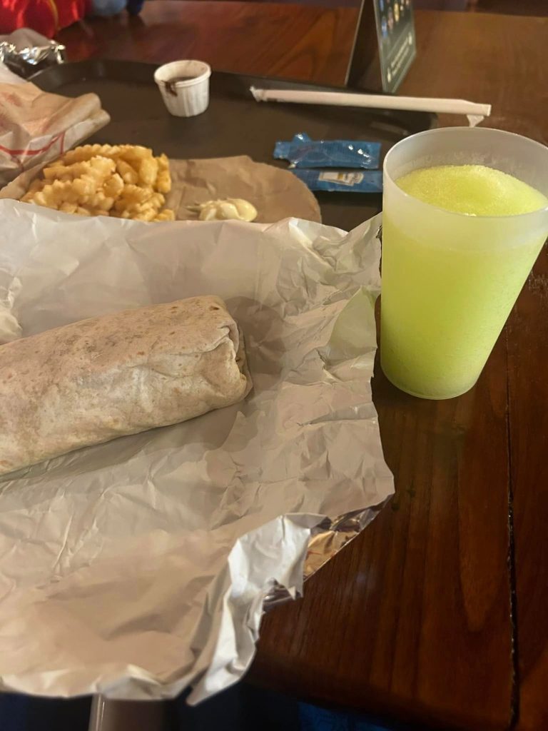 Image shows a takeaway wrapper with a burrito on it and a plastic cup filled with a yellow ide slush