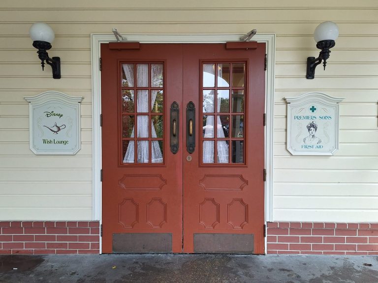 Image showing a double wooden door to a building with lamps by each side and signs for first aid and wish lounge