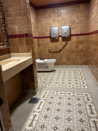 a large tiled accessible bathroom with a toilet, grab rail, and sink