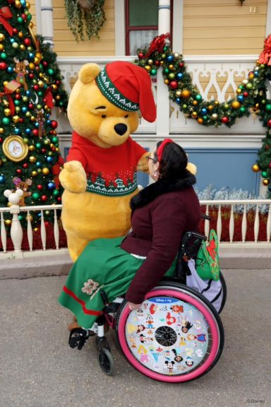 Jody is seated in her chair and is approaching winnie the pooh wearing a Christmas jumper 