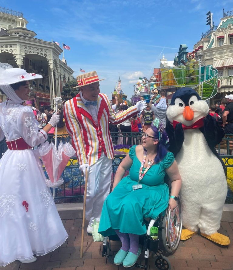 Image shows Jody meeting Mary Poppins, Bert and a penquin on main street, with the castle in the background