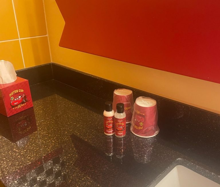 Image of the side of the sink which is a black worktop with some miniature toiletry bottles and wrapped cups, along with a box of tissues all themed to cars