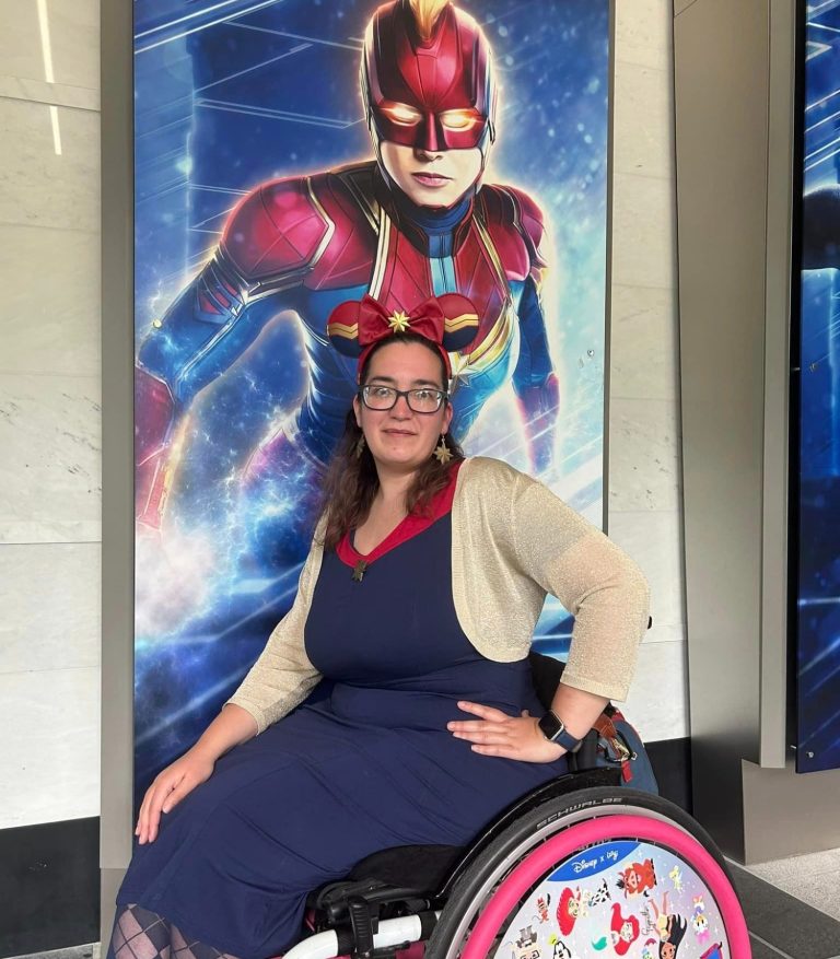 Image of jody seated in her chair wearing a navy pencil dress with captain marvel ears