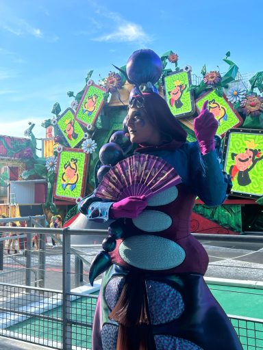 A performer dressed in blue and purple and holding a fan