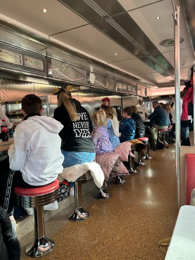 there are a number of people seated on stools against a retro style diner counter