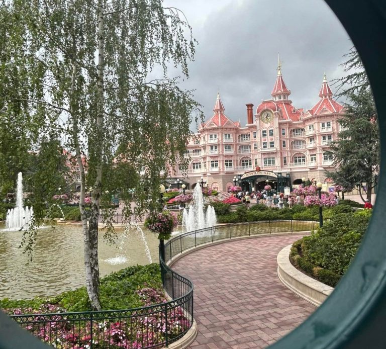 Image of the Disneyland Hotel, a large pink Victorian style building, with paved gardens and fountains in front of it