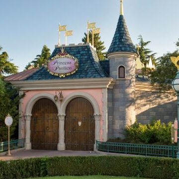 An image of the exterior of the princess pavilion, a pink building with a turret and blue tiled roof and large wooden doors