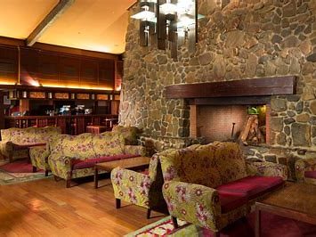 Image shows a cosy bar area with stone walls, wood floors, rugs, couches and a fire