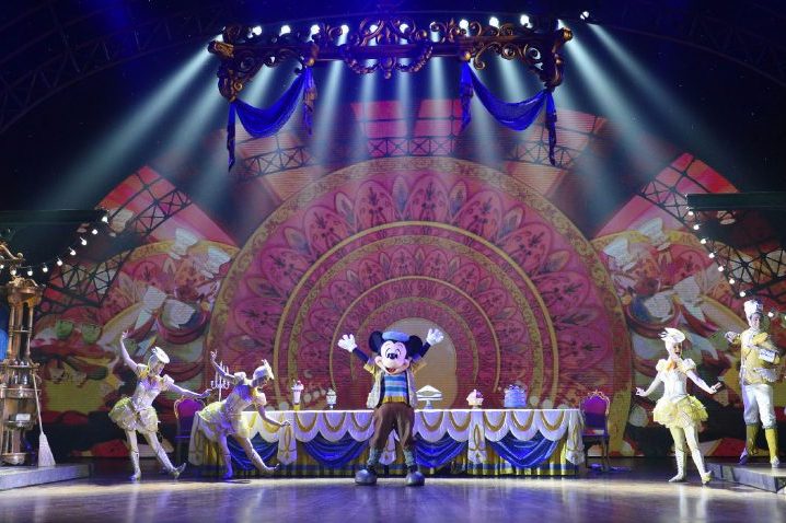 The image shows some of the cast on stage, including Mickey and dancers themed to be our guest from beauty and the beast