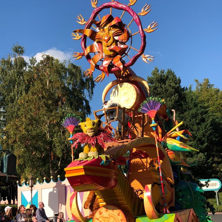 The image shows a lion king float in the parade with lots of orange and brown decorations and simba featuring