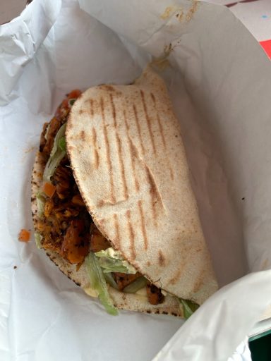 a folded pita on a paper wrapper, you can see a hint of salad and fake meat inside the folded pita