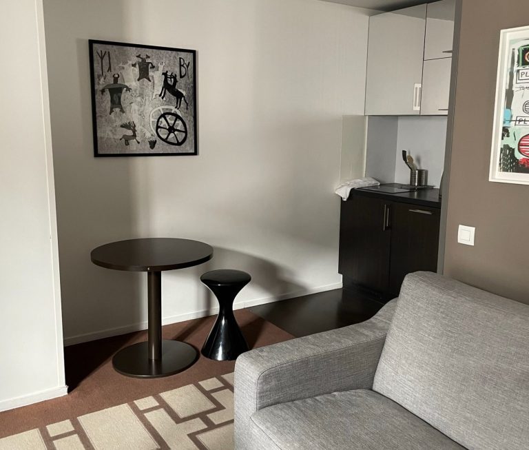 Image of an area of the room with a sofa and then a table and the kitchenette area