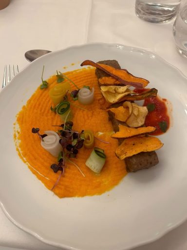 Image of food on a plate, an orange puree and vegetable crisps