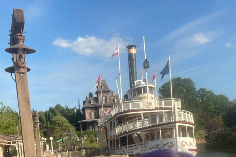 Image shows the Molly Brown white steamer style boat with Phantom Manor in the Background