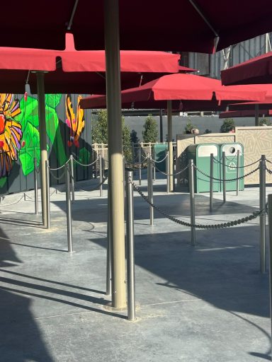 A paved queue line with metal ropes and large red umbrellas