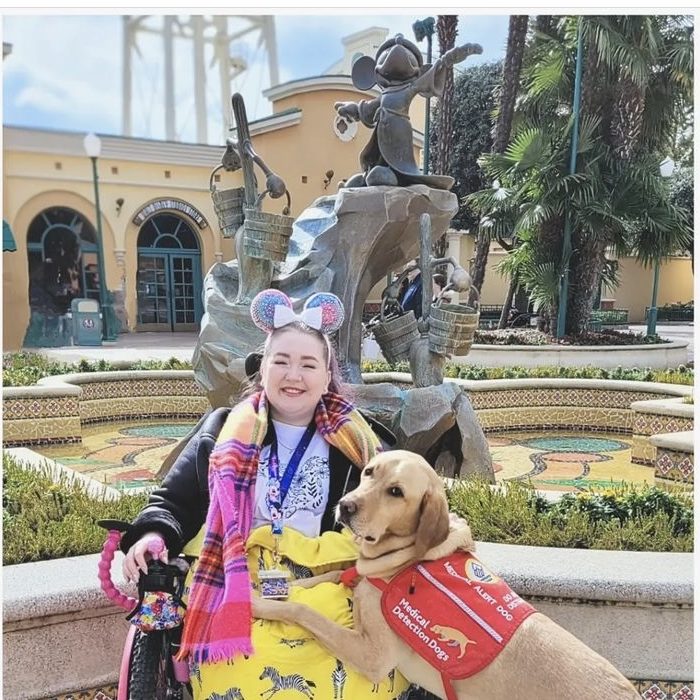 Image of lizzy in her chair seated next to her assistance dog henry