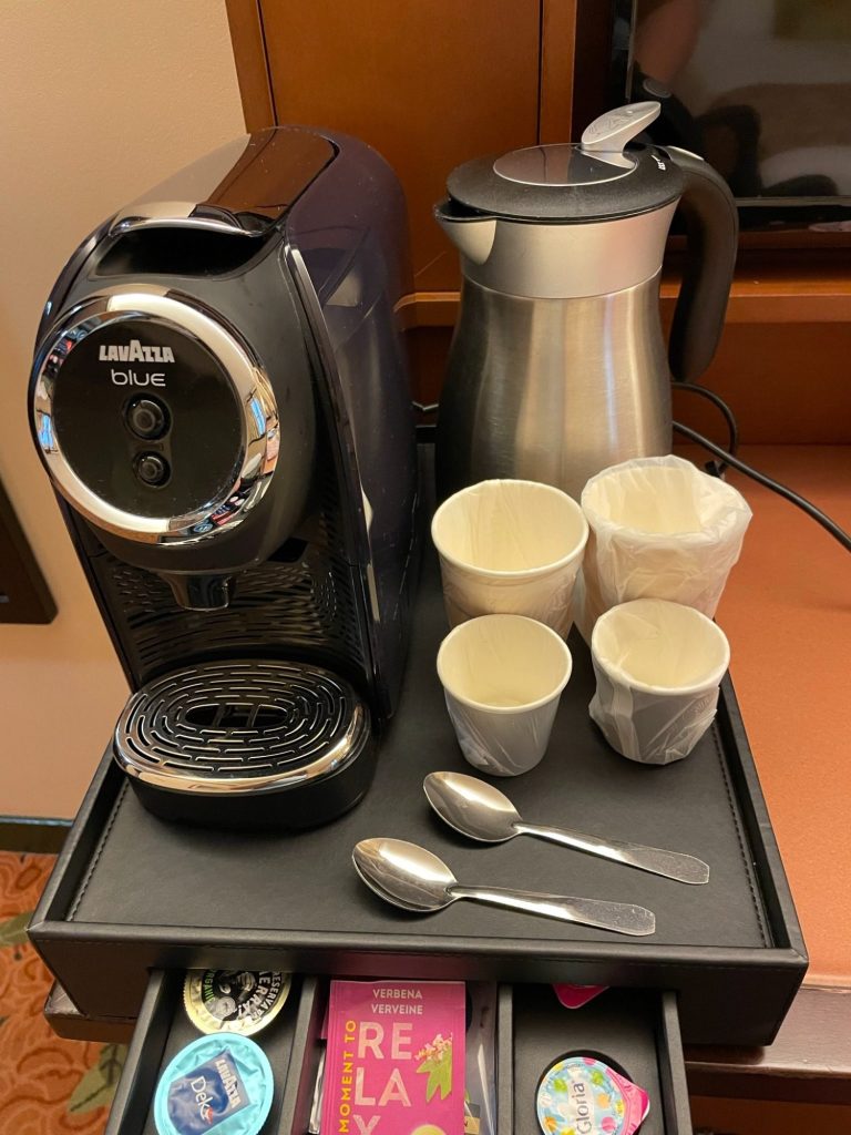 Image of a kettle and coffee machine with some paper cups and spoons and some pods and teabags