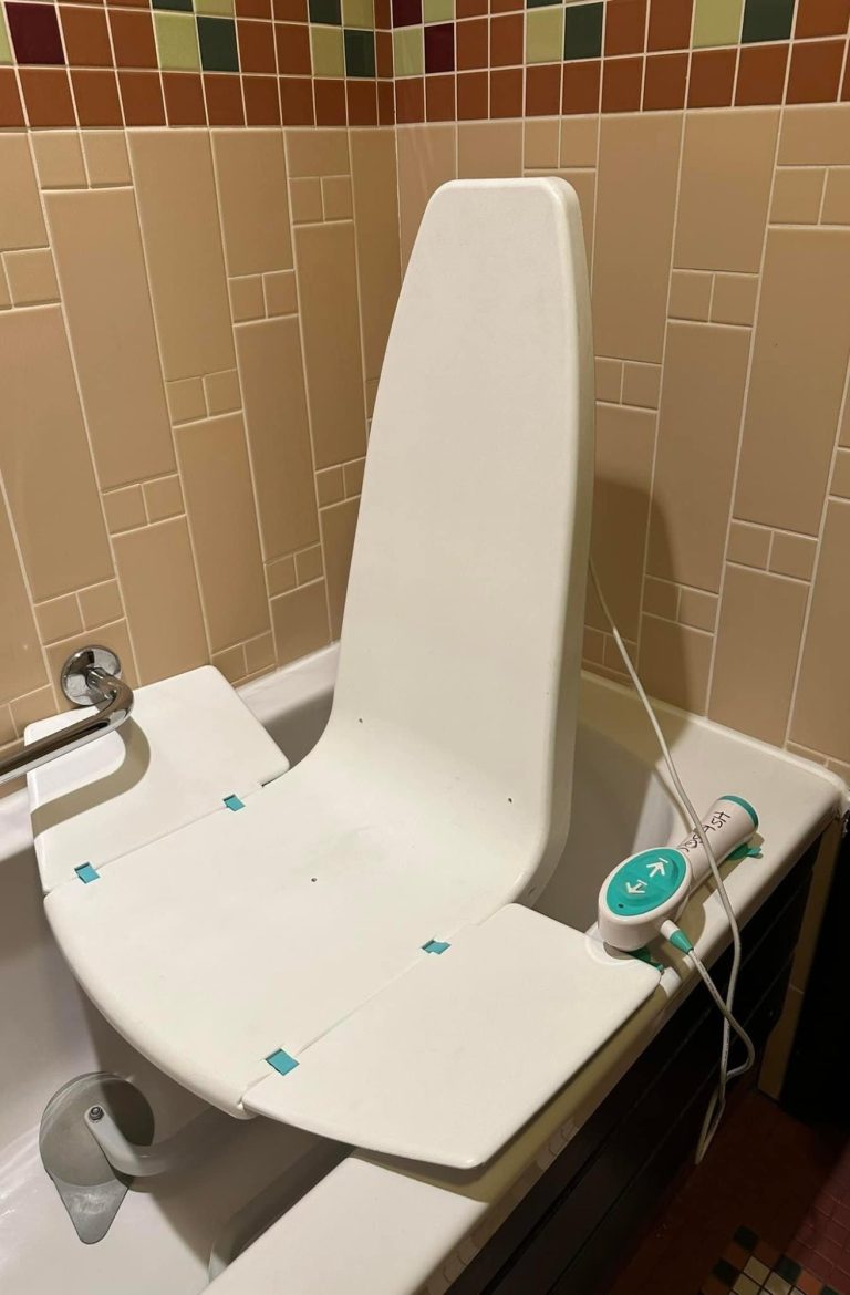 Image of a bath seat used in a standard bath, it is white and fits within the bath and can rise up to transfer to bath