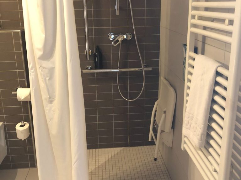 Image of the wetroom shower area with a shower curtain, fold down shower seat and some grabrails