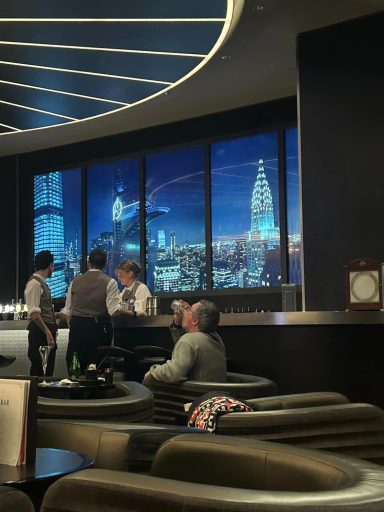 there is a bar area with large screens behind it giving the appearance of the new york skyline