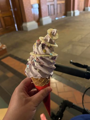 Omage shows a pale purple whippy ice cream in a waffle cone with shite chocolate rings on top