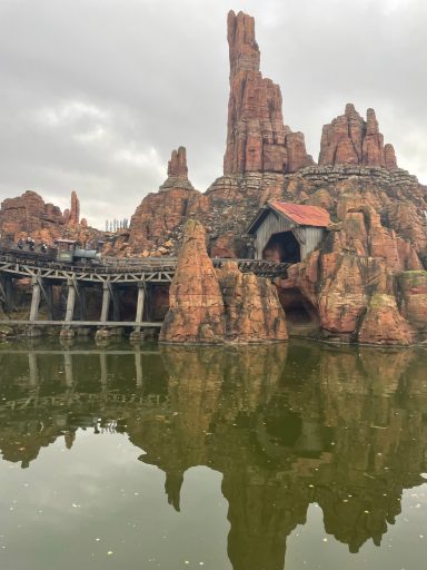 Image shows a rocky outcrop in a lake with antrance in the rock and a train track leading into it, reminiscent of the wild west desserts