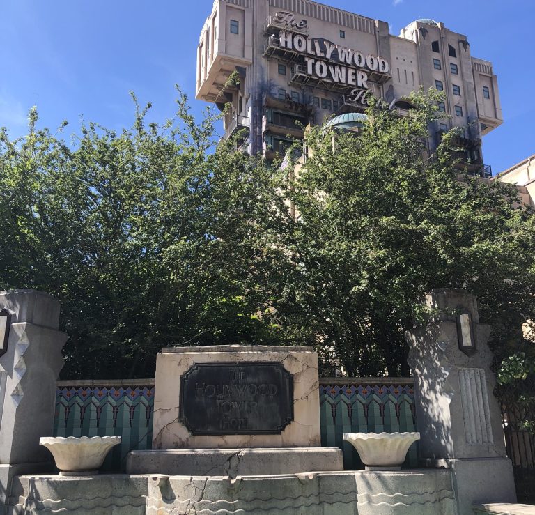 Photo of the outside of the ride area with dilapidated fountain, fence and the large tower hotel in the background