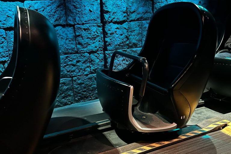 Image shows the ride vehicle which is black, seats two people on a bench seat then has a high curved back and sides and a lap bar