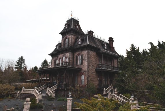 Image shows a dilapidated looking manor house positioned in a hill with stone staircases leading up to it