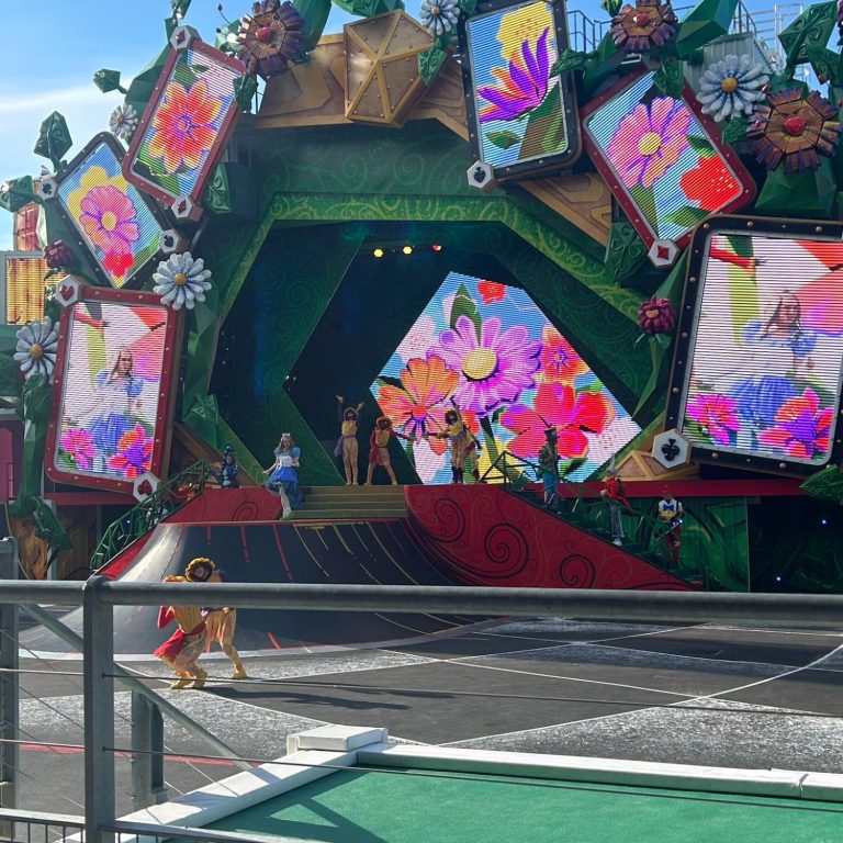 Image of a a stage with vibrant colourful flowers and large screens