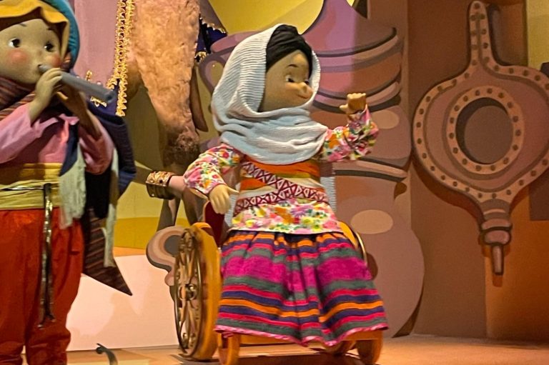 Image showing a close up of one of the wheelchair using dolls, the doll is wearing a headscarf and a colourful striped skirt