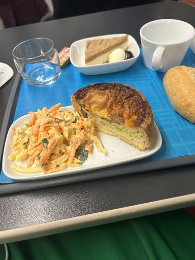 Image of some food items on a tray inclusing a cup, bread roll, quiche and dessert