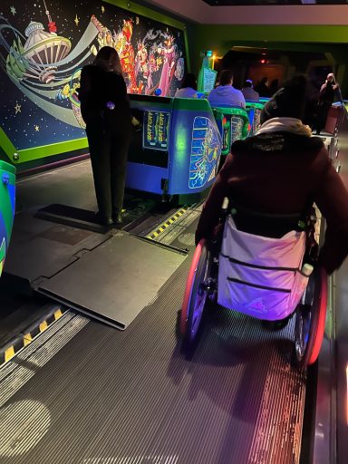 image of a wheelchair user about to roll up a ramp into a buzz lightyear vehicle