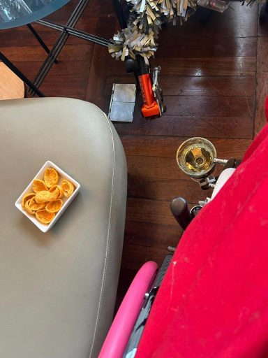 Image of a small bowl of crisp snacks and the side of a wheelchair with a cupholder holding a glass of wine