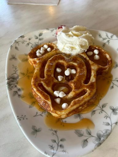 A waffle that is shaped liked mickeys head, with whipped cream and a caramel sauce