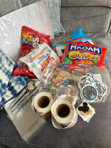 Image shows a pile of bags of sweets, some rolls of stickers and loose stickers and some packets containing button badges