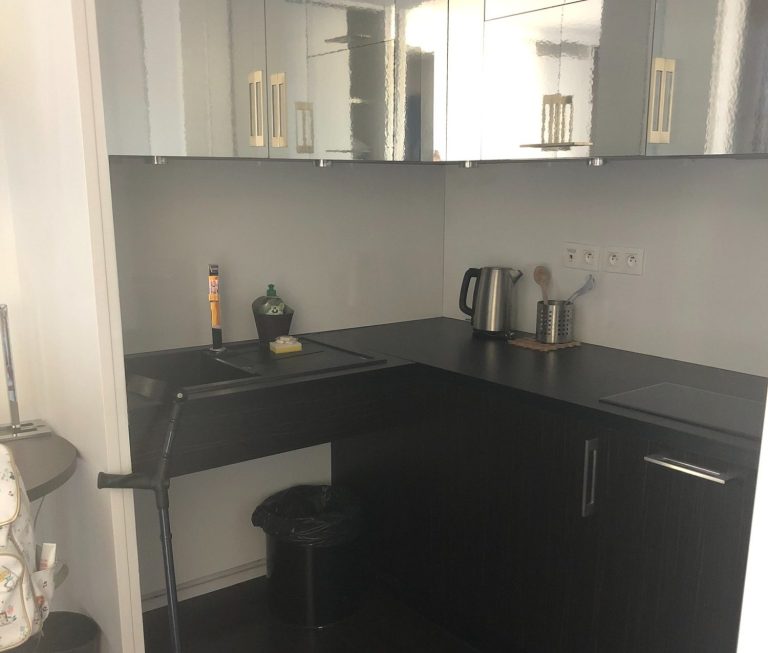 Image of kitchen area with dark cupboards and counters, you can see a sink and kettle