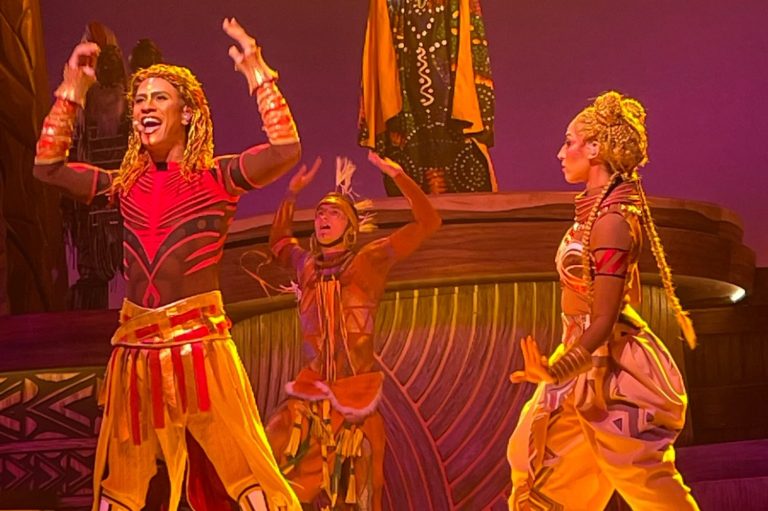 The image shows Simba and Nala in the show wearing African inspired costumes